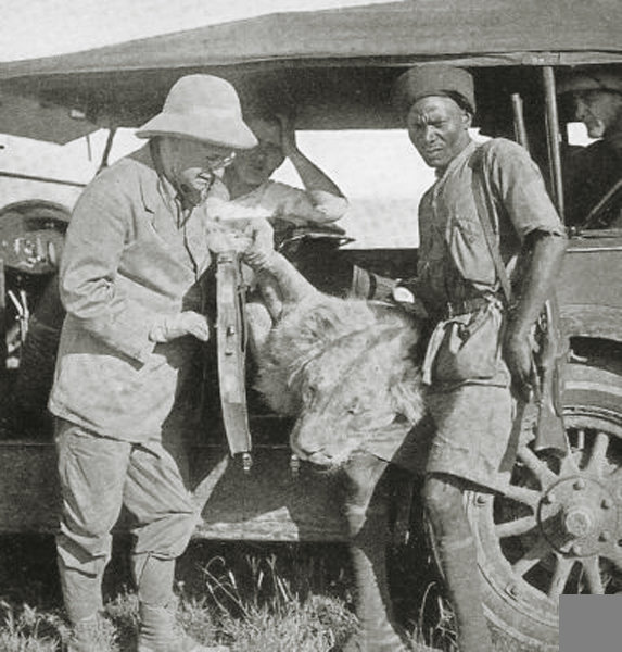 British East Africa hunter and askari with dead lion in the safari vehicle  1920.jpg